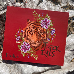 Red box with tiger illustration, floral accents, and "Tiger Eyes" text on a sequin surface