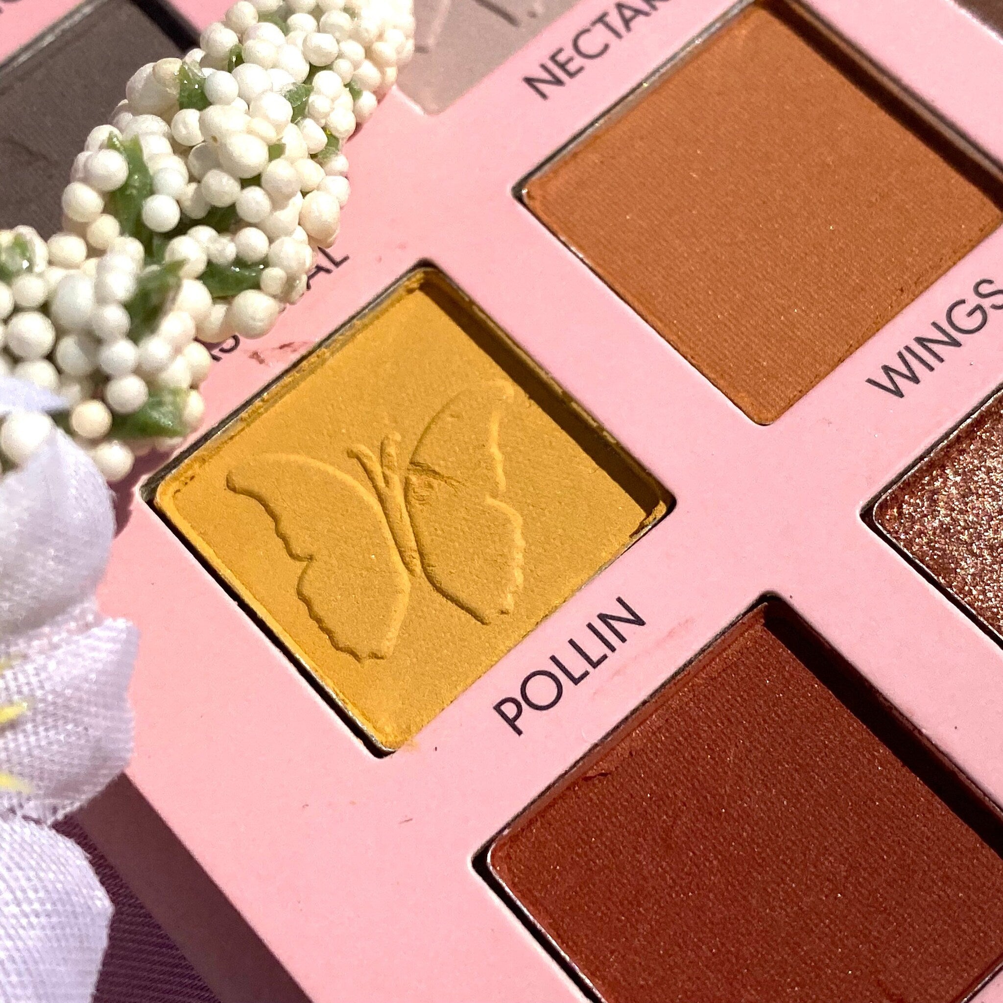 Eyeshadow palette with yellow, brown, and pink shades, butterfly design, and floral accent.