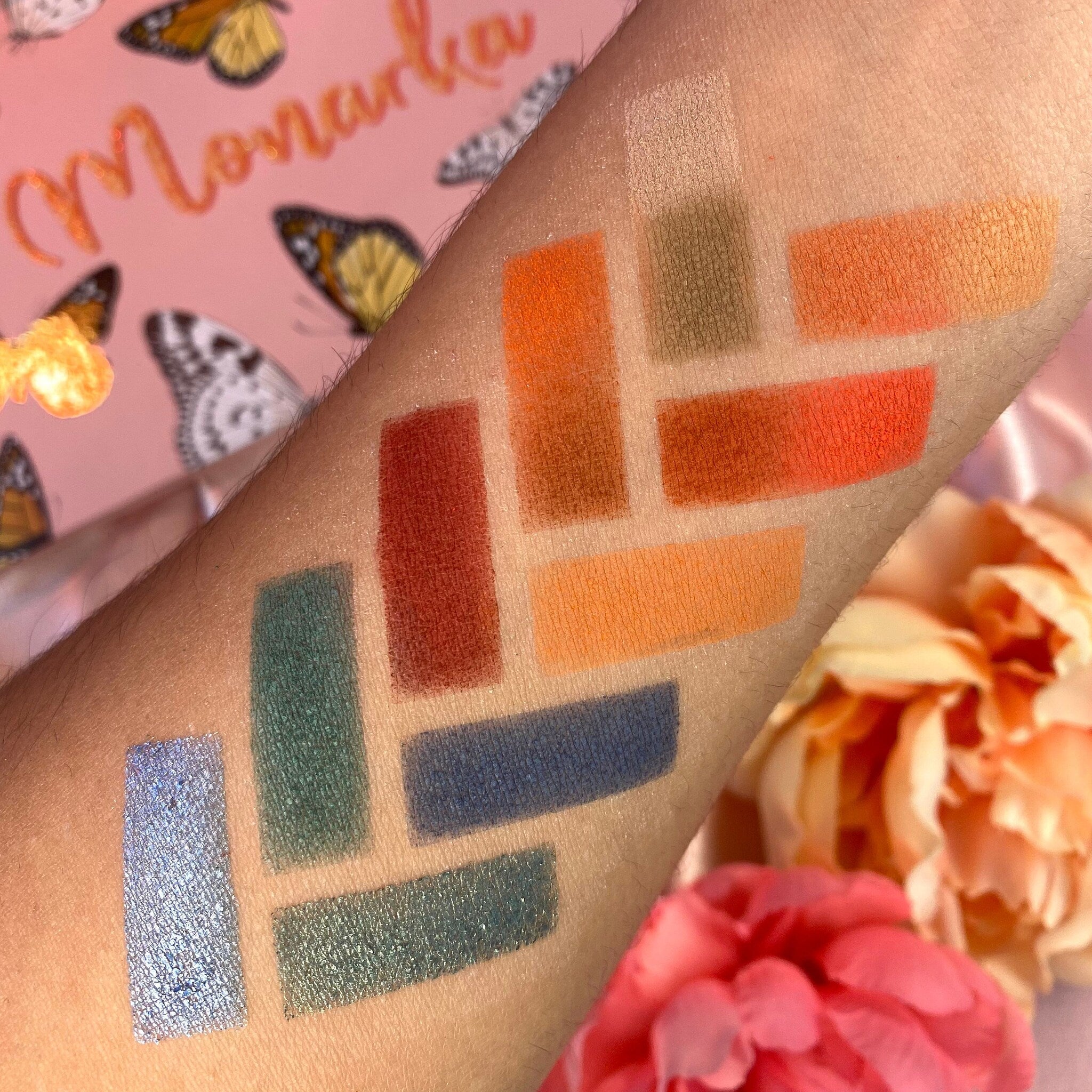 Eyeshadow swatches in orange, blue, and green shades on skin, Monarcha brand name visible
