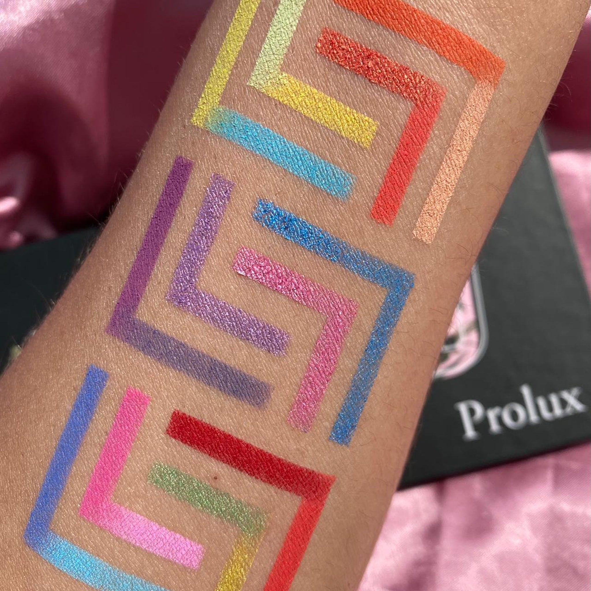 Colorful Prolux eyeshadow swatches on arm, geometric pattern, various shades
