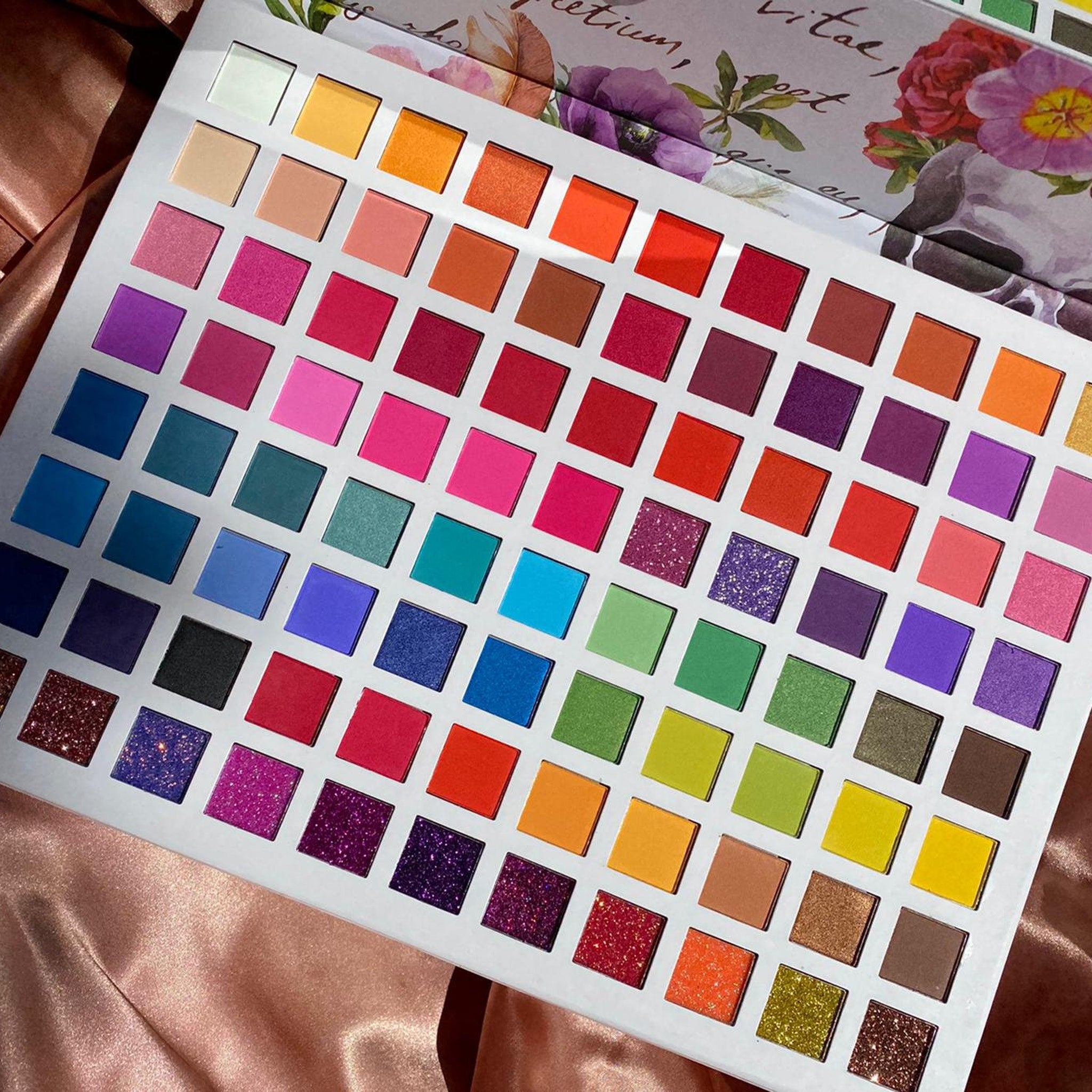 Eyeshadow palette with multiple colors, square pans, and floral design on the cover