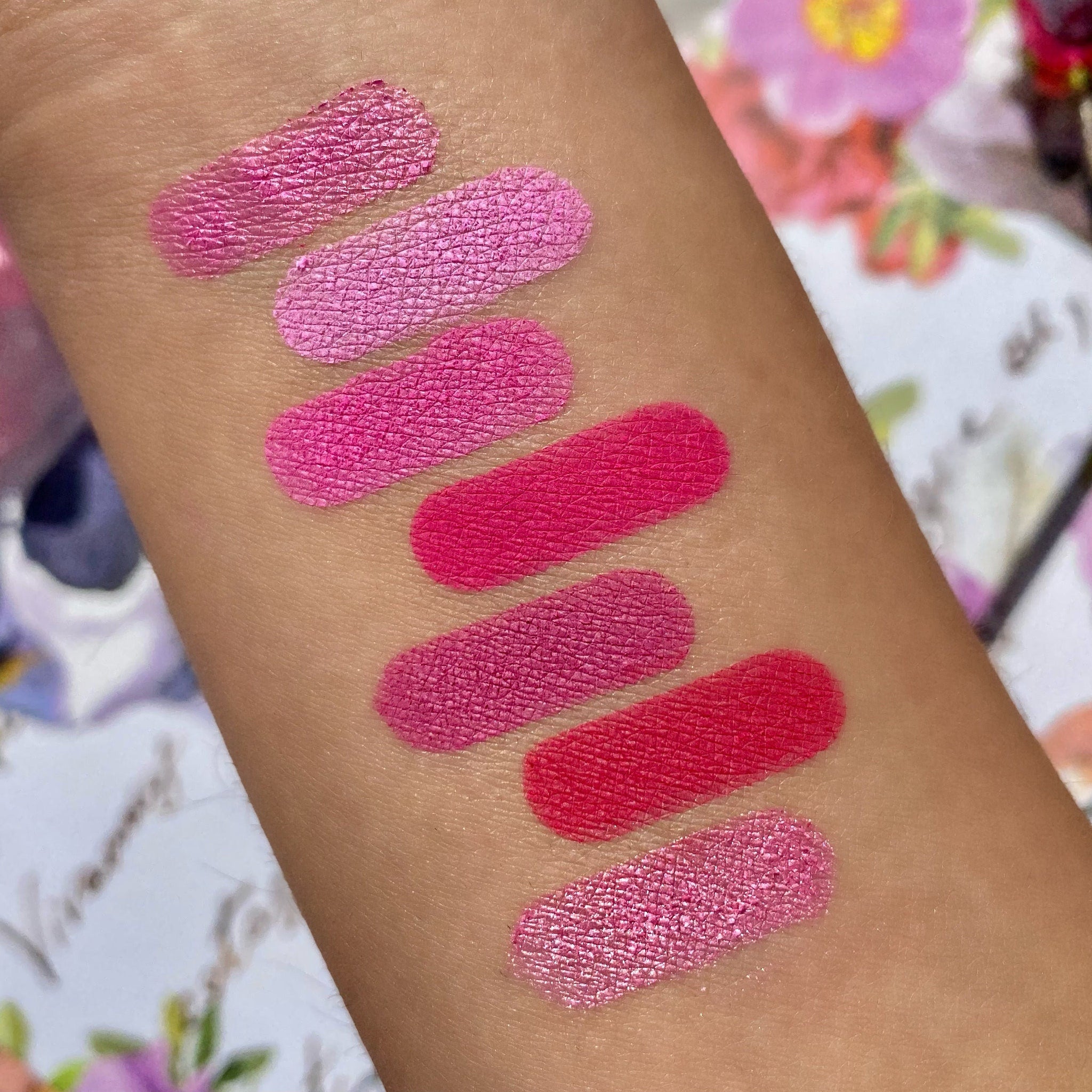 Lipstick swatches in pink and red shades on arm, with textured finish and various colors
