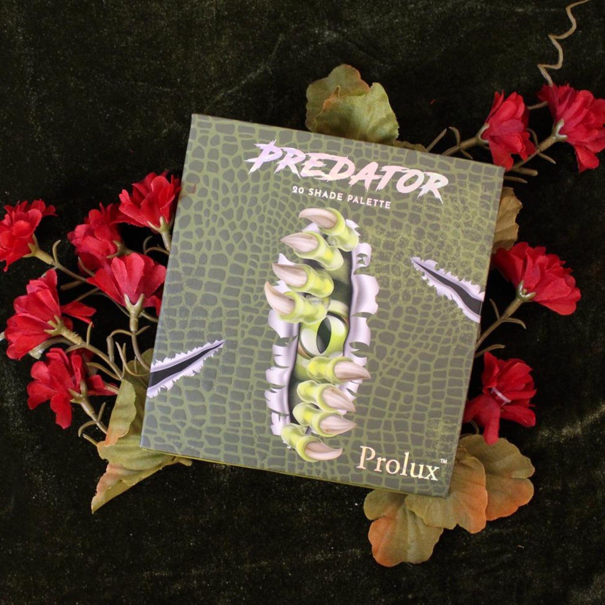 Eyeshadow palette with green reptile pattern, "Predator" text, and red floral accents.