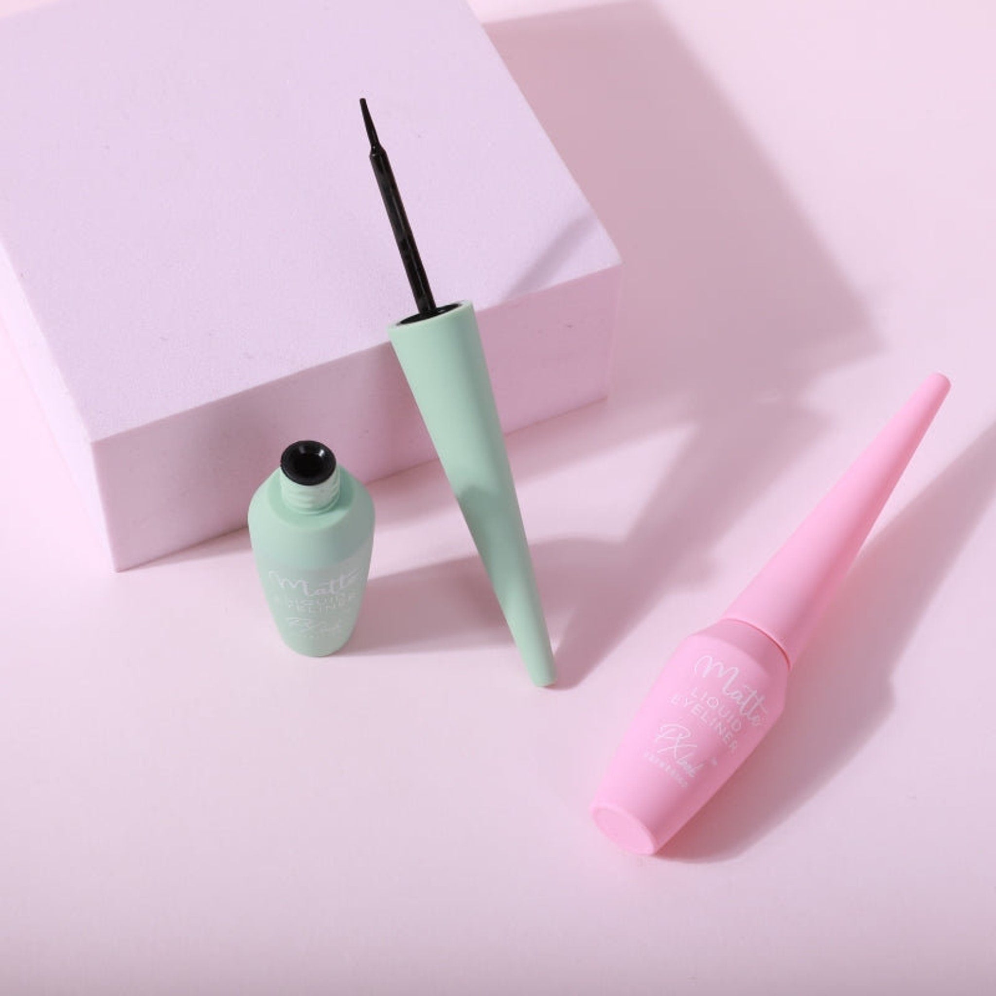 Liquid eyeliner in mint green and pink with black applicator, "Matte" text visible