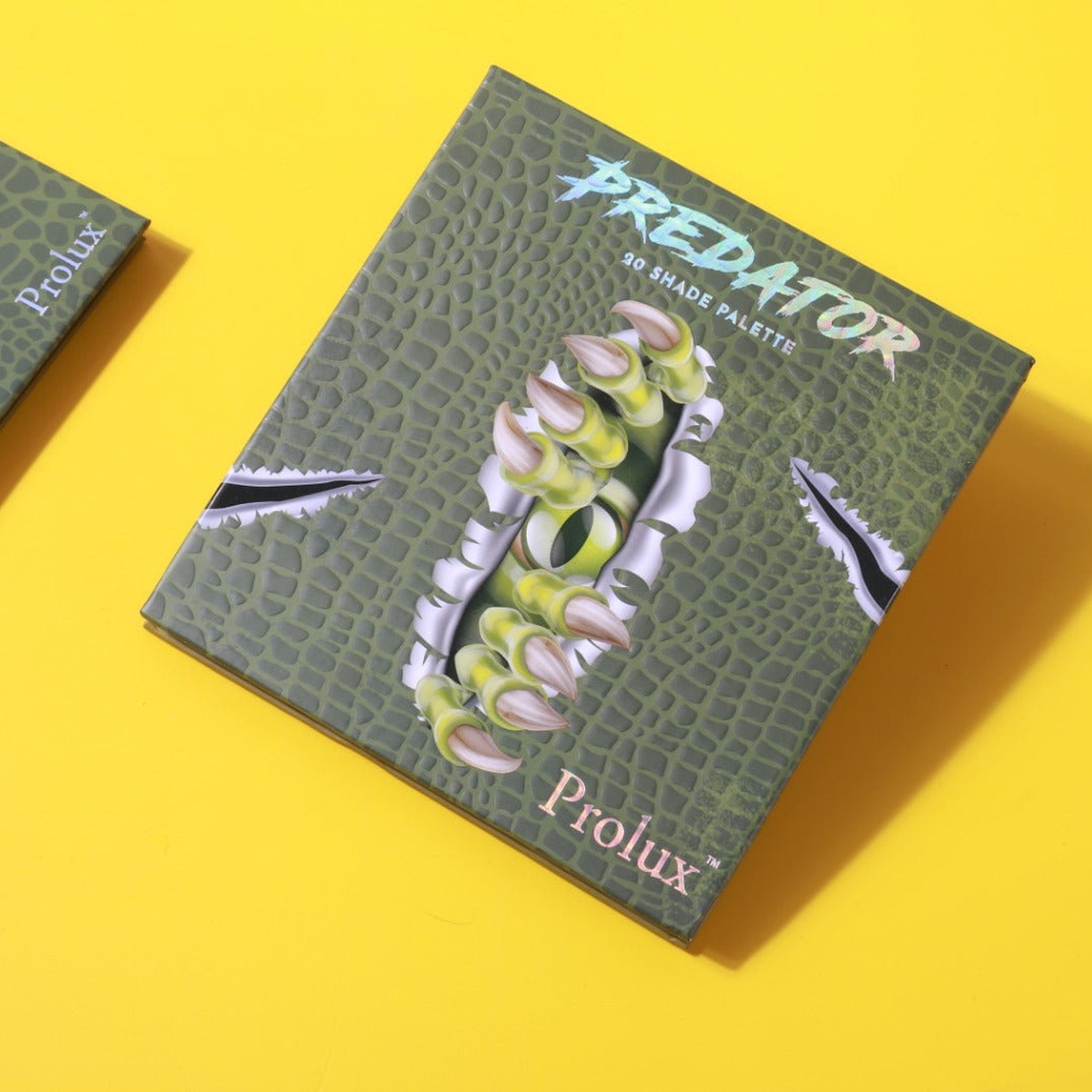 Eyeshadow palette with green reptile pattern, "Predator" text, and Prolux brand name on yellow background