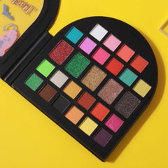 Eyeshadow palette with multiple colors, glitter, and matte shades in a black case on yellow background