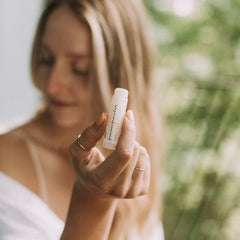 Lip balm tube, white with black text, held in hand with gold rings