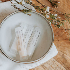 Lip balm tubes in white with text, inside a ceramic bowl on a wooden surface