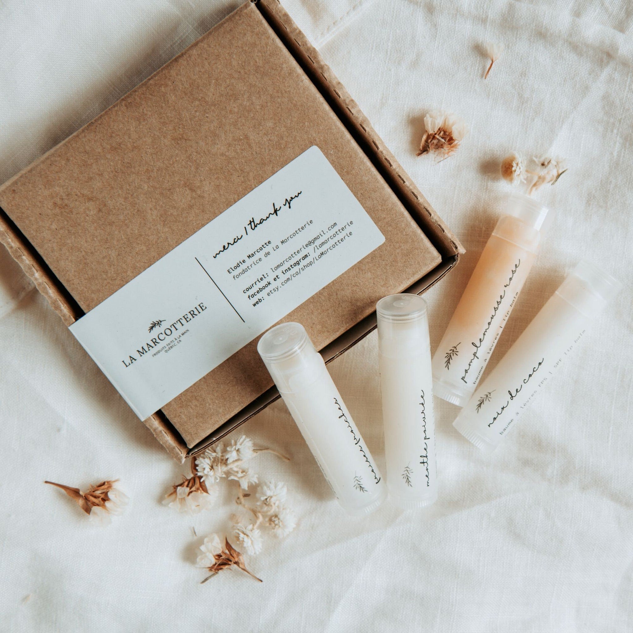 Lip balm set with clear tubes, brown box, and La Marcotterie branding on white fabric