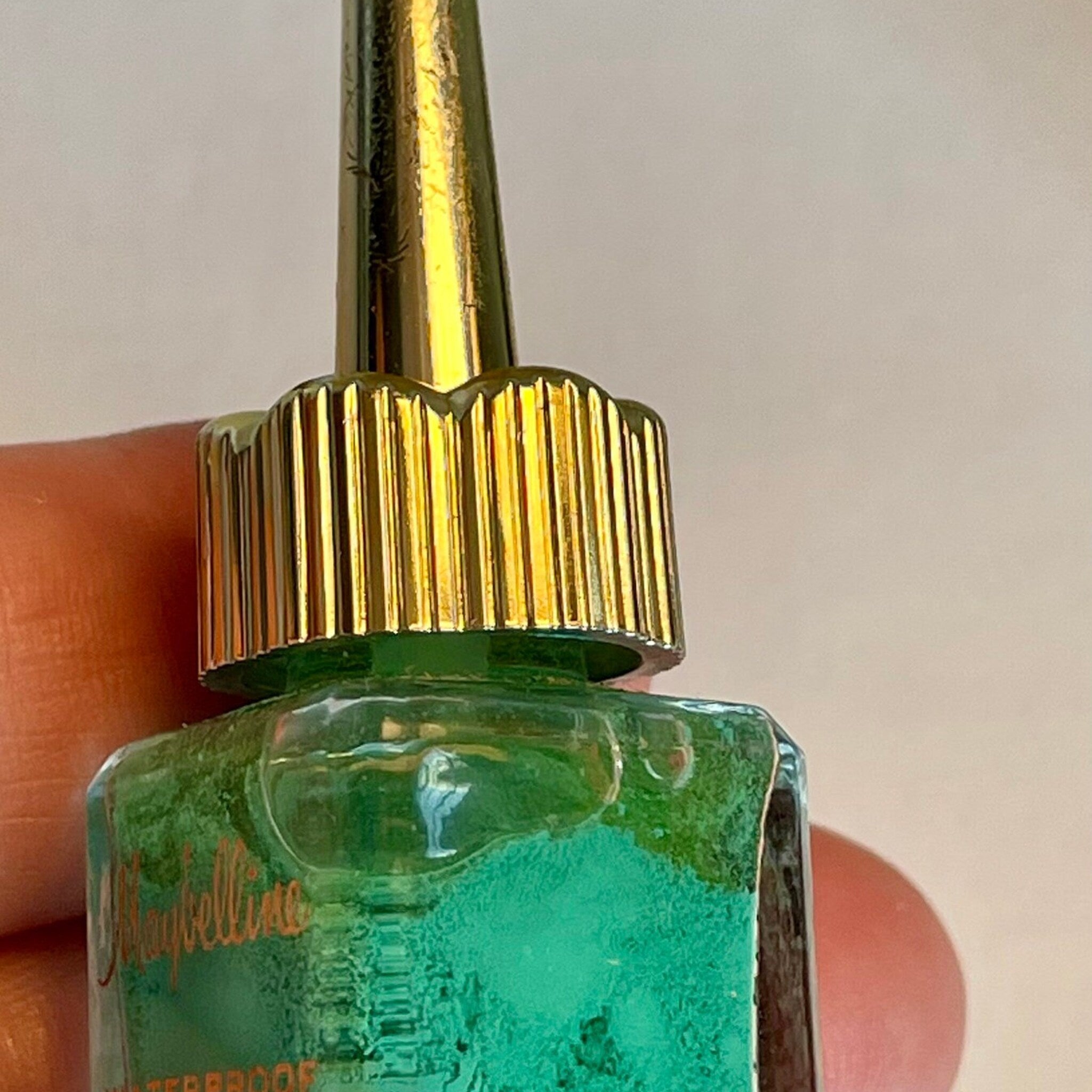 Side view of vintage green eyeliner in glass bottle with golden spire lid, showcasing tapered shape and retro branding