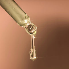 Dropper with clear liquid, glass, and a single drop falling against a brown background