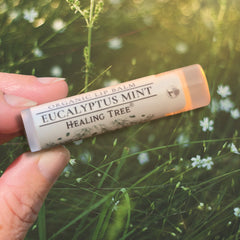 Lip balm tube with white and orange packaging, "Eucalyptus Mint" text, held by hand