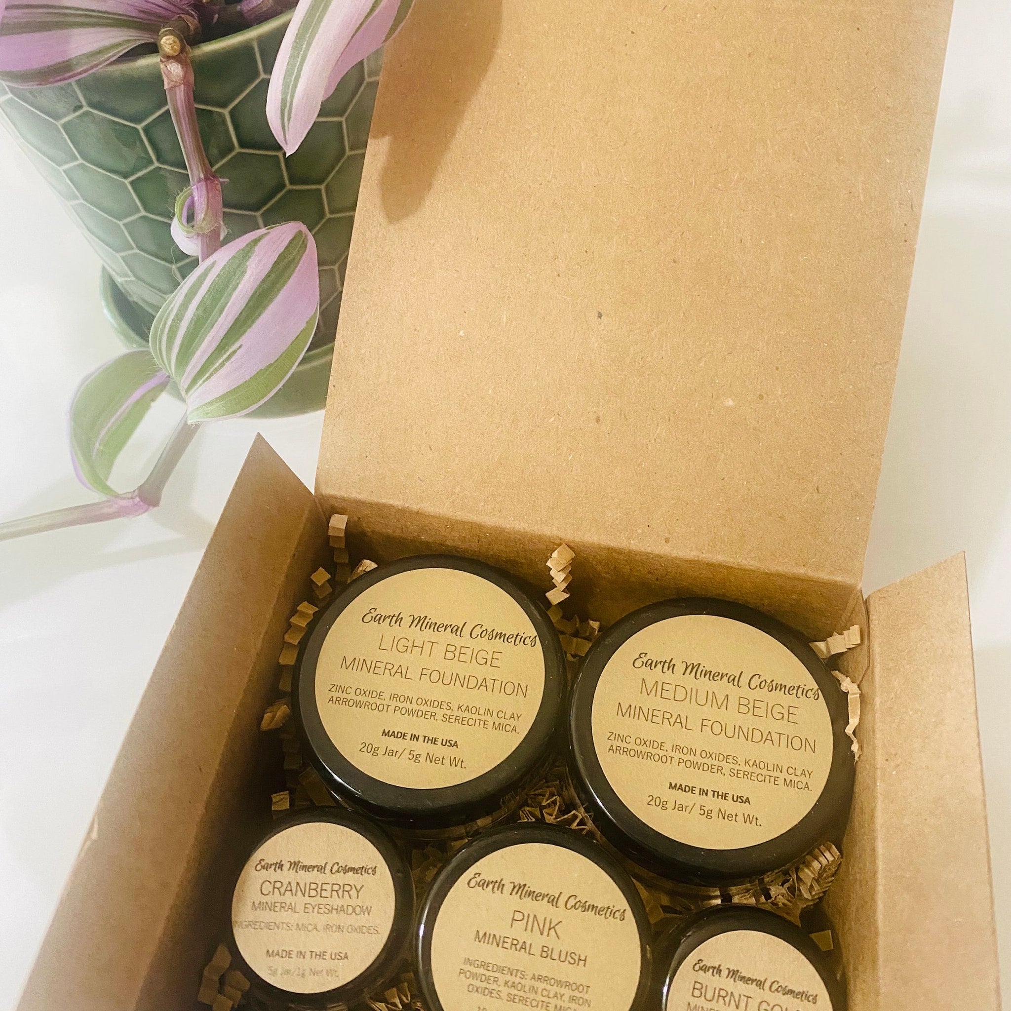 Mineral makeup jars in a brown cardboard box with Earth Mineral Cosmetics label visible