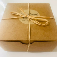 Gift box tied with raffia, brown cardboard, and brand name on label.