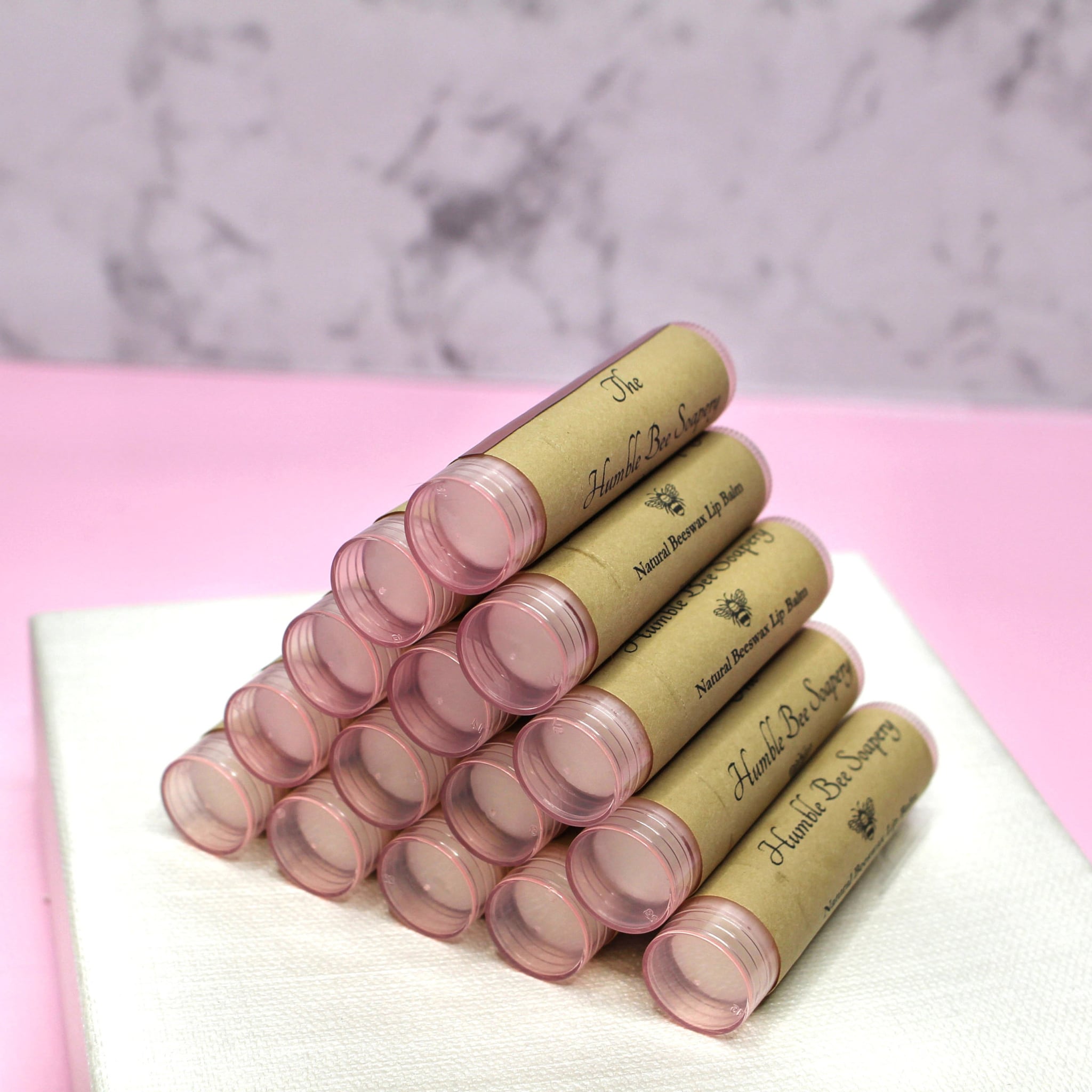 Lip balm tubes with brown paper labels, pink plastic tops, and Humble Bee Soapery text stacked together