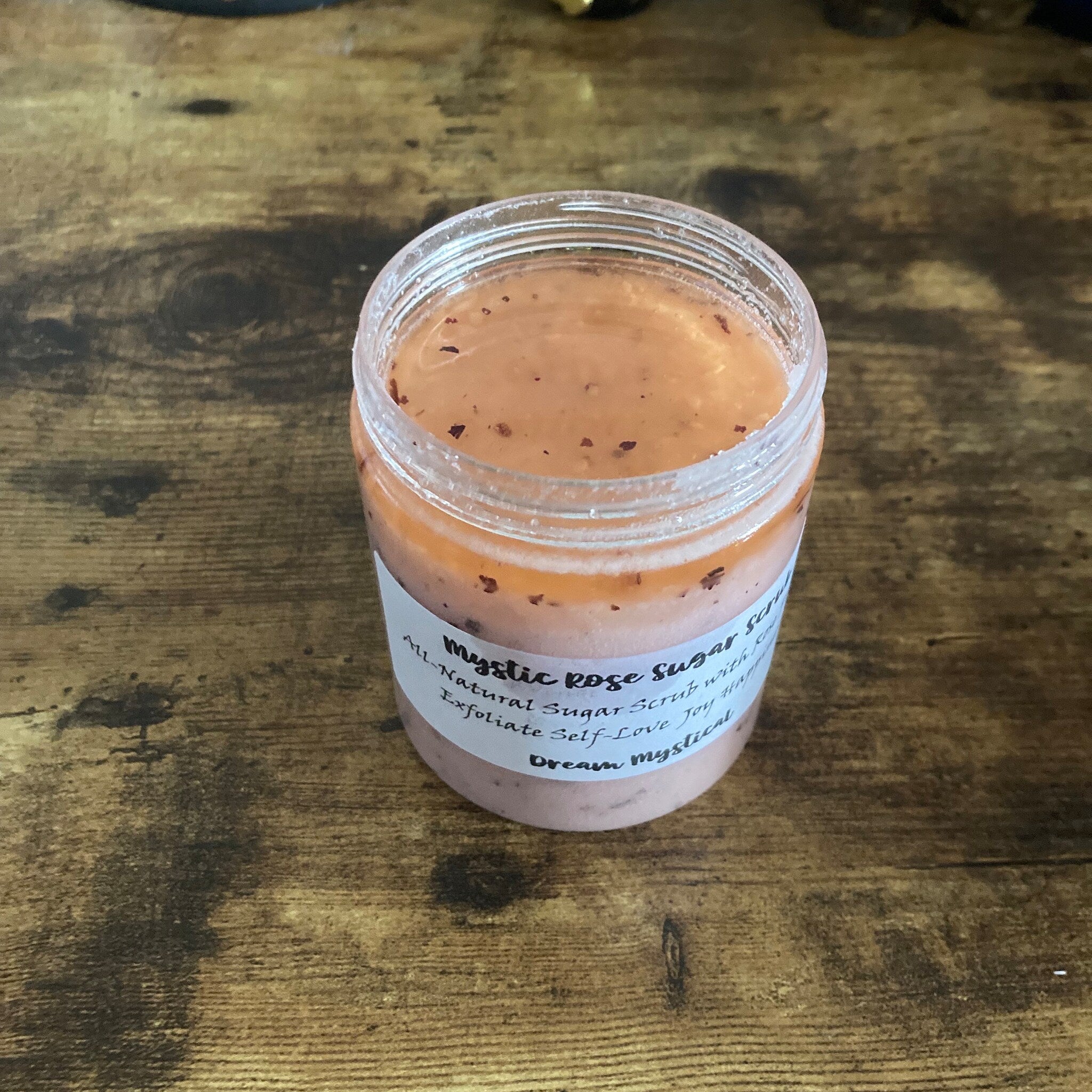 Sugar scrub jar with pink and orange contents, clear plastic container, and white label with text visible