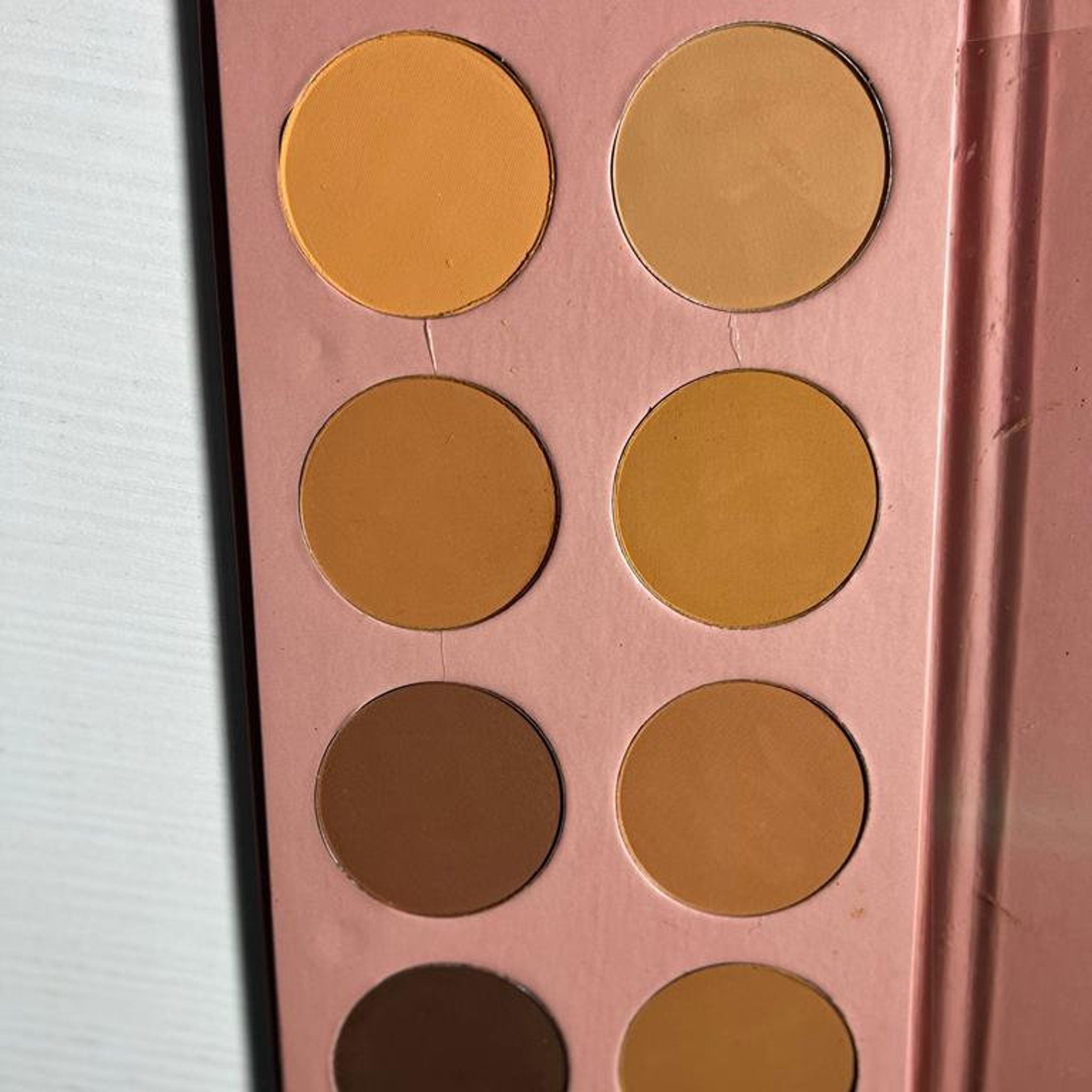 Eyeshadow palette with multiple shades of brown and tan in a pink case