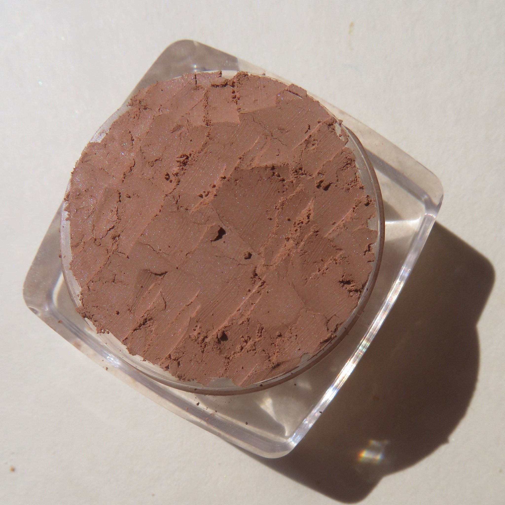 Hand applying matte brown loose powder eyeshadow with brush for a soft, blended look on eyelid