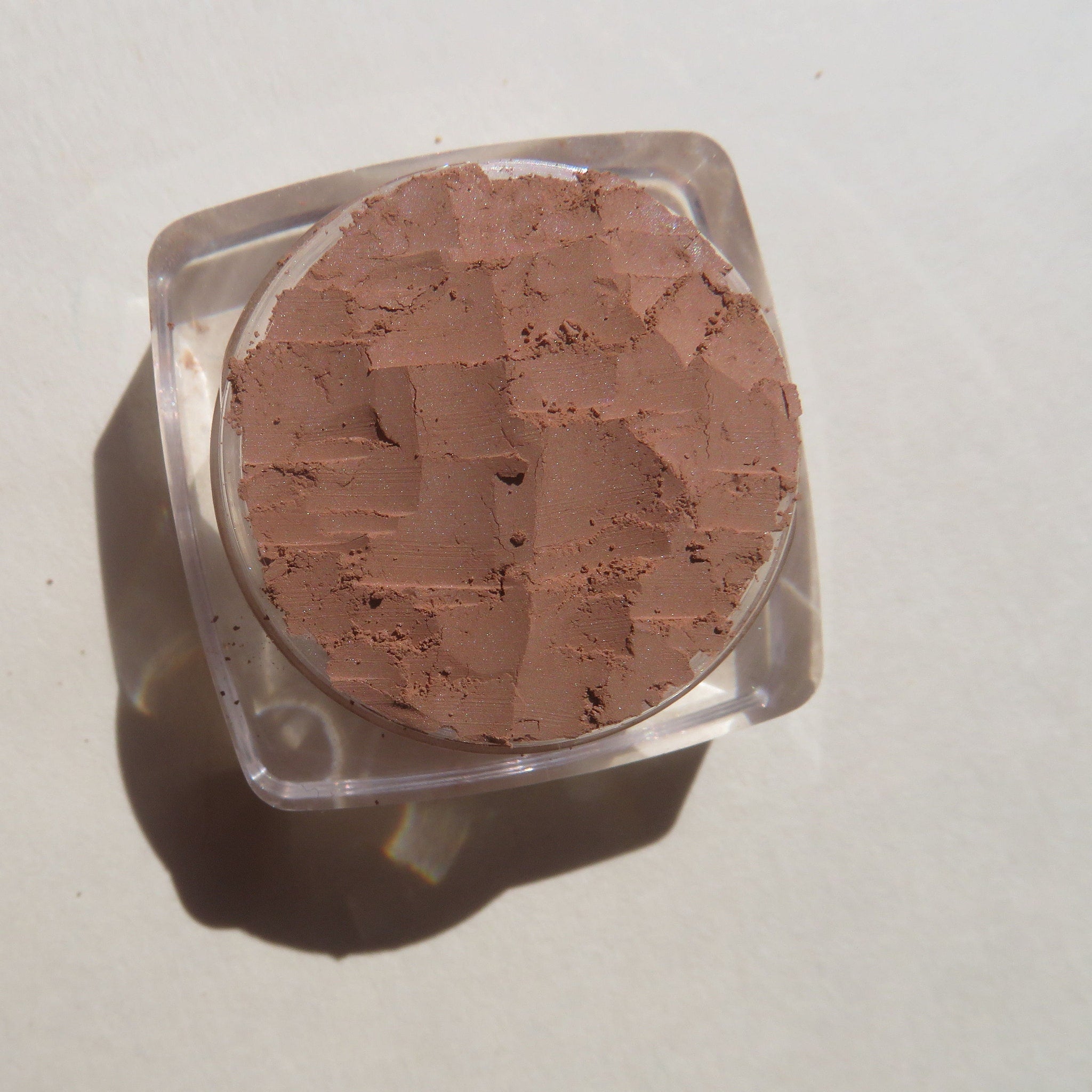 Close-up of matte brown loose mineral eyeshadow powder spilling from container onto surface