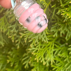 Clear glass and pink spiral-shaped object held by a person over green foliage background