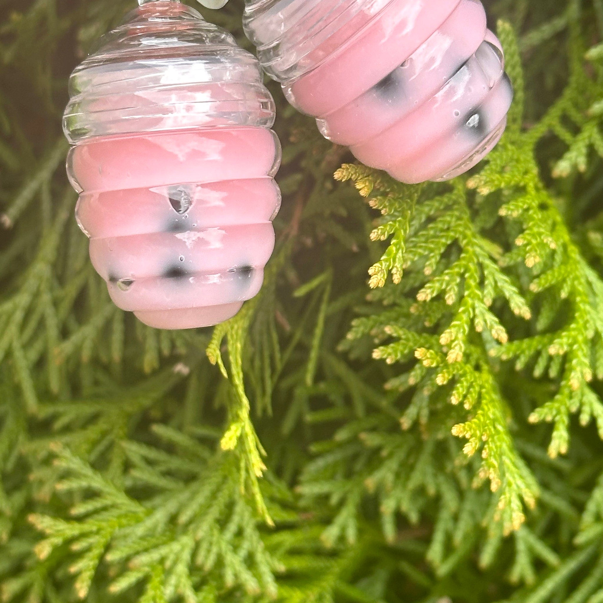 Pink and clear glass ornaments with black specks, on green foliage background
