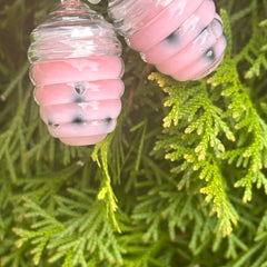 Pink and clear glass ornaments with black specks, on green foliage background