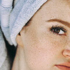 Eye with long lashes, freckled skin, and blue towel in close-up shot