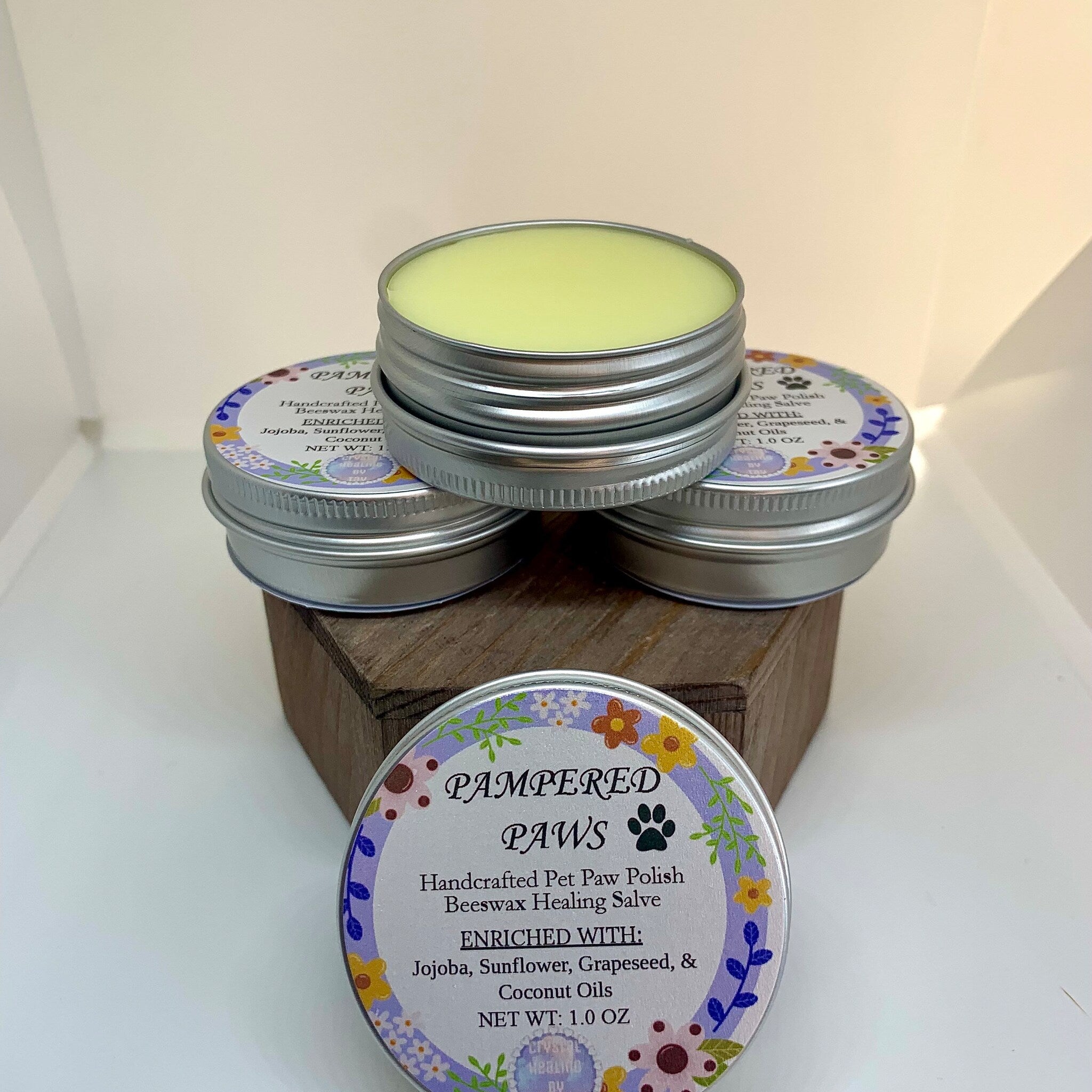 Pet paw healing salve in metal tins with floral label, stacked on wood block, by Pampered Paws