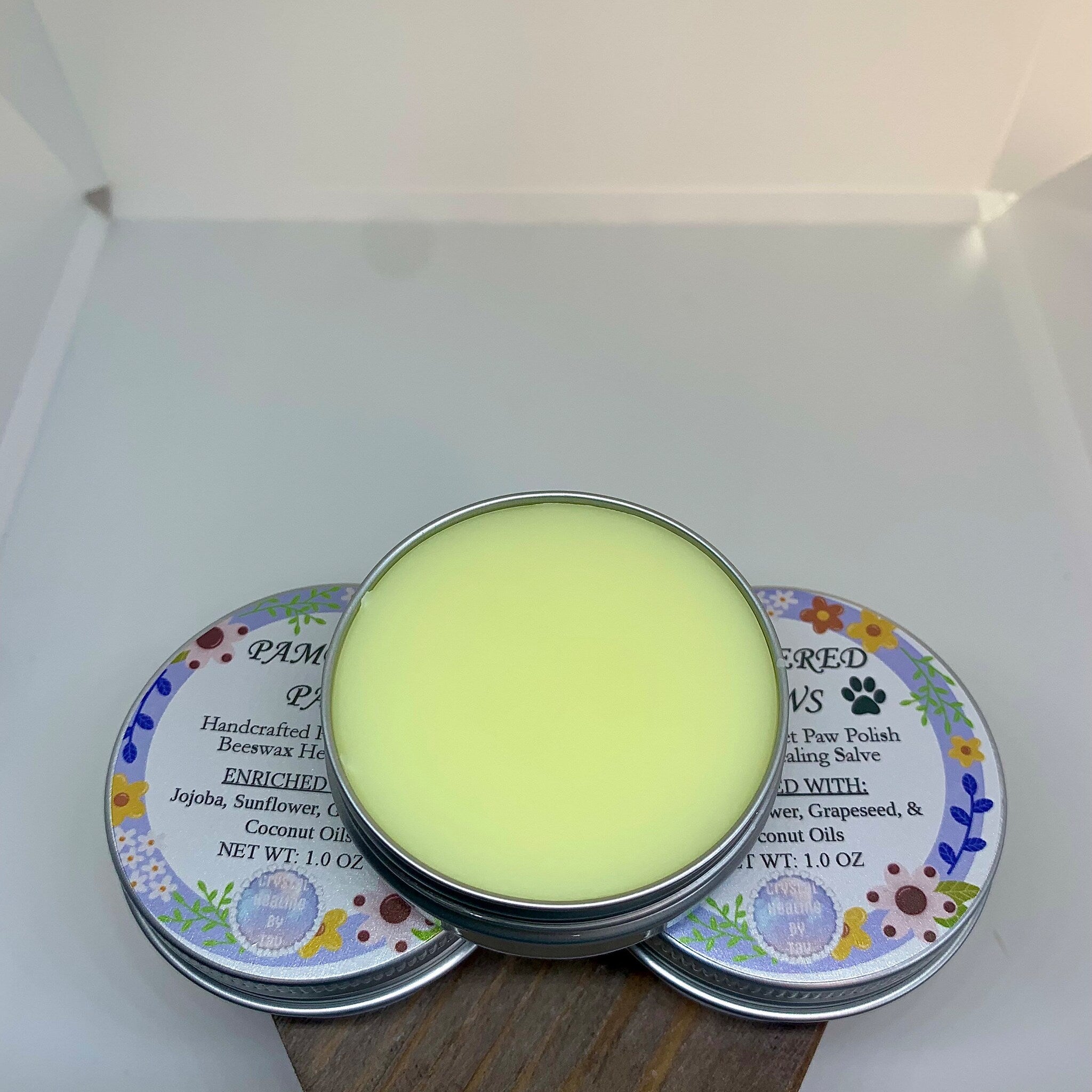 Paw salve with light green balm, silver tin, and floral label design with text