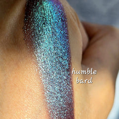 Close-up of fingertips applying shimmery multichrome eye shadow with color-shifting sparkles on eyelid