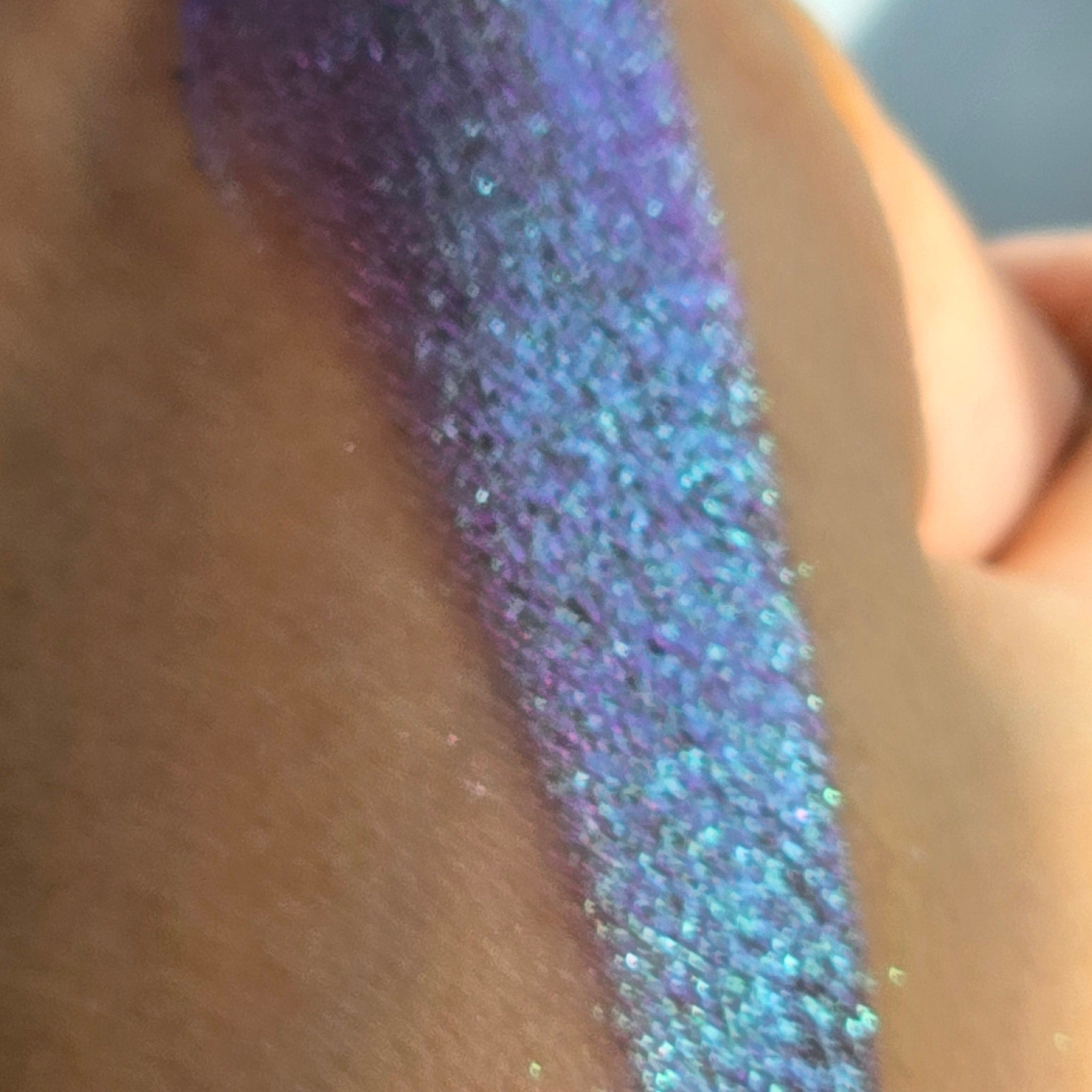 Side view of Humble Bard multichrome eye shadow showing shimmery color shift from teal to purple in angled lighting
