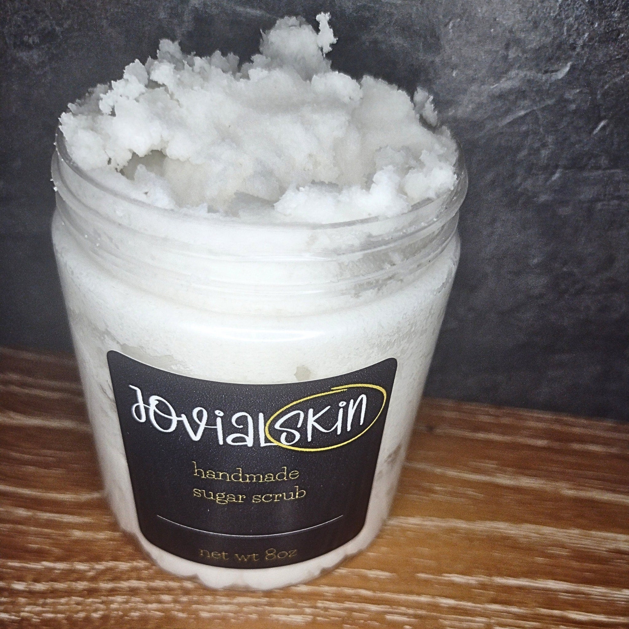 Sugar scrub in clear jar with white granules, Jovial Skin label, and black background