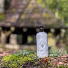Body lotion bottle with white label, black pump, and "RAINIER" text on mossy log