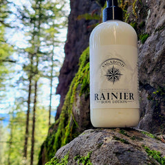 Body lotion bottle with white label, black pump, and "Rainier" text on a rock