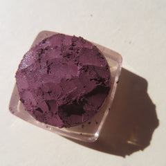 Close-up of dark purple shimmer vegan mineral eye shadow with loose pigment texture and eco-friendly packaging