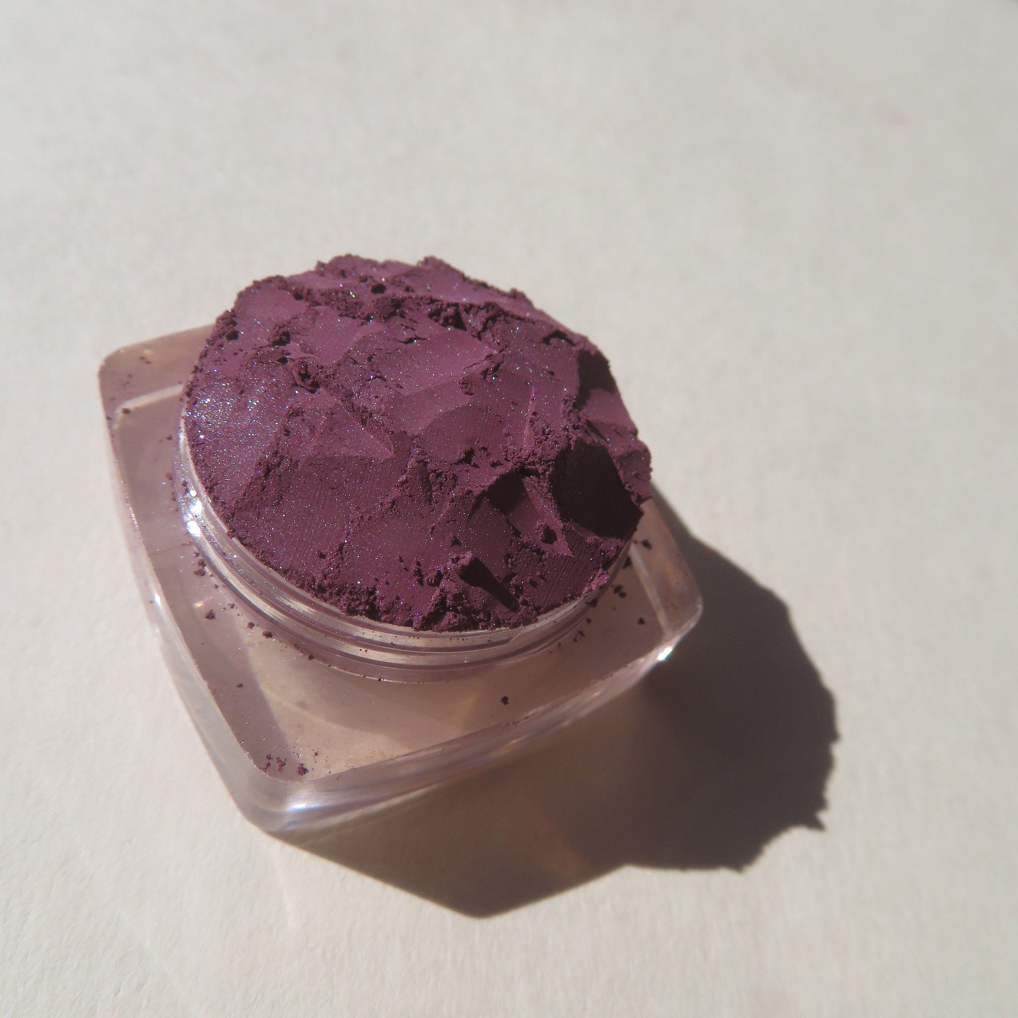 Side view of dark purple shimmer loose mineral eyeshadow in eco-friendly packaging, showcasing vibrant pigment dispersion