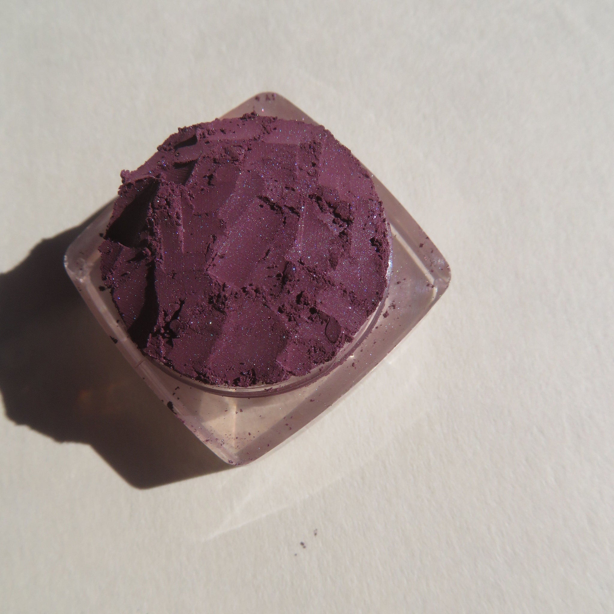 Hand applying dark purple shimmer vegan mineral eye shadow with fingertip, showcasing loose pigment texture and rich color payoff