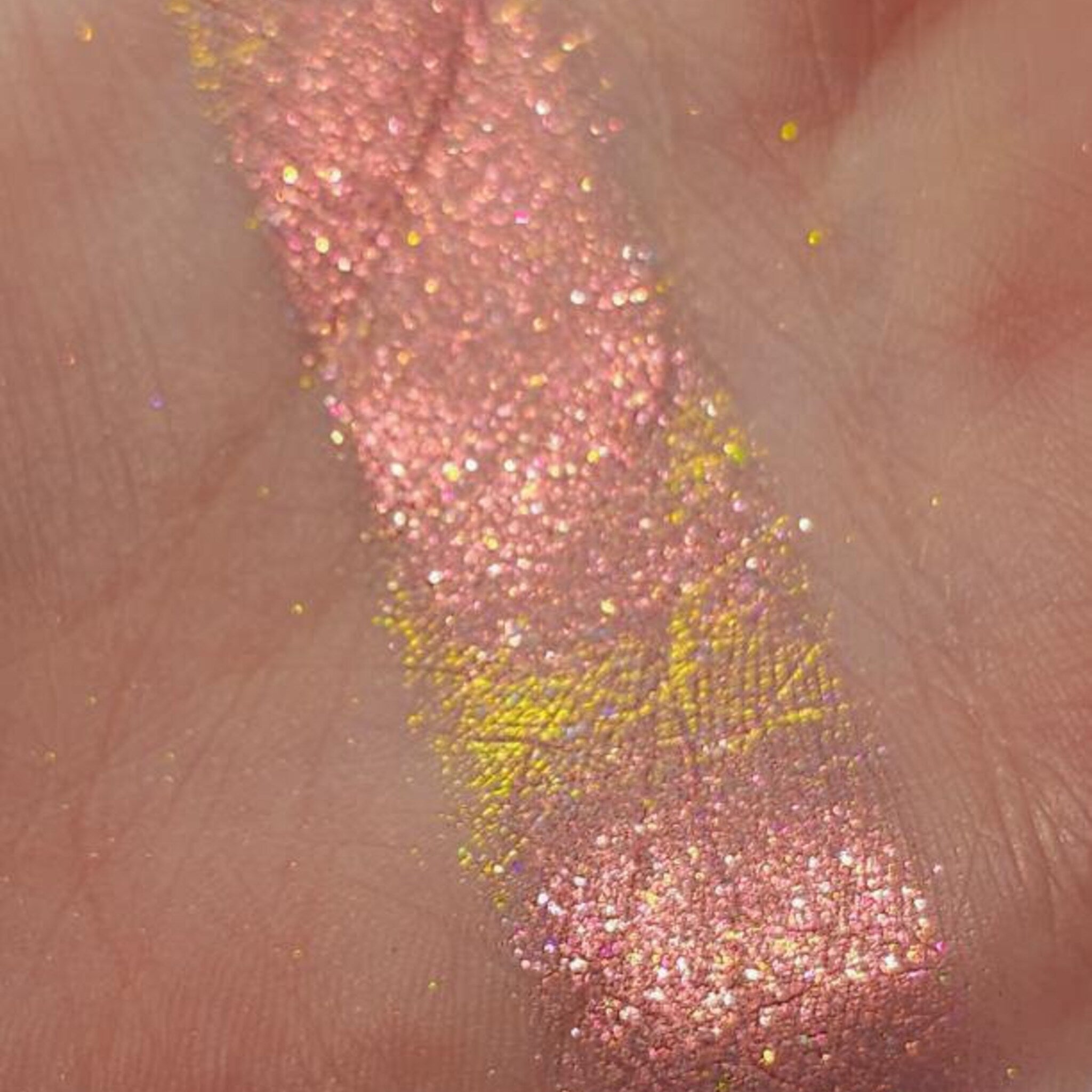 Close-up of fingertips applying shimmery pink and gold eye shadow to eyelid with blending brush
