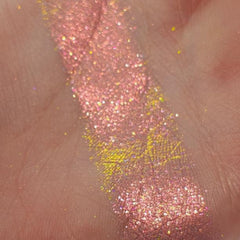 Close-up of fingertips applying shimmery pink and gold eye shadow to eyelid with blending brush