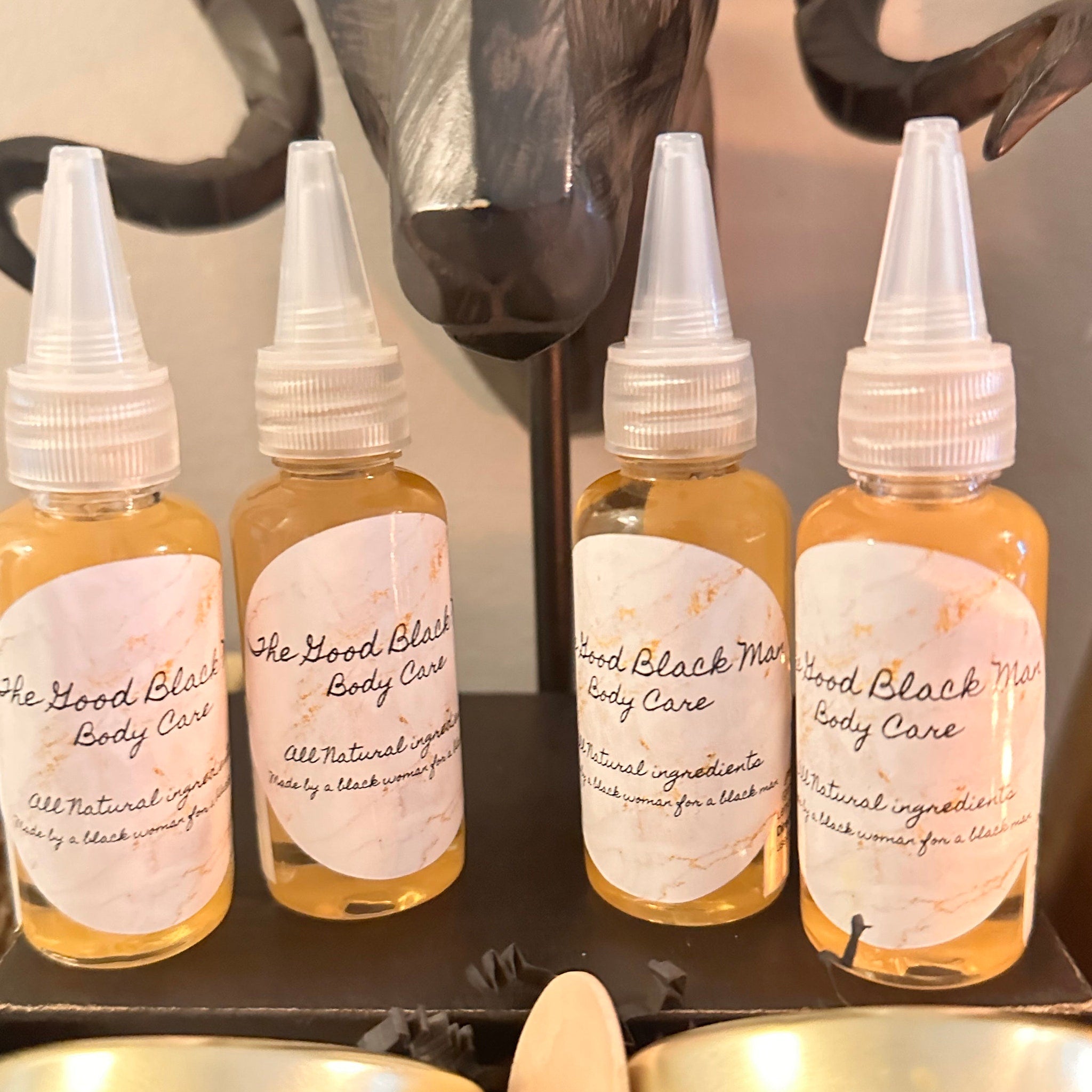 Body care bottles with clear plastic tops, amber liquid, and "The Good Black Body Care" label