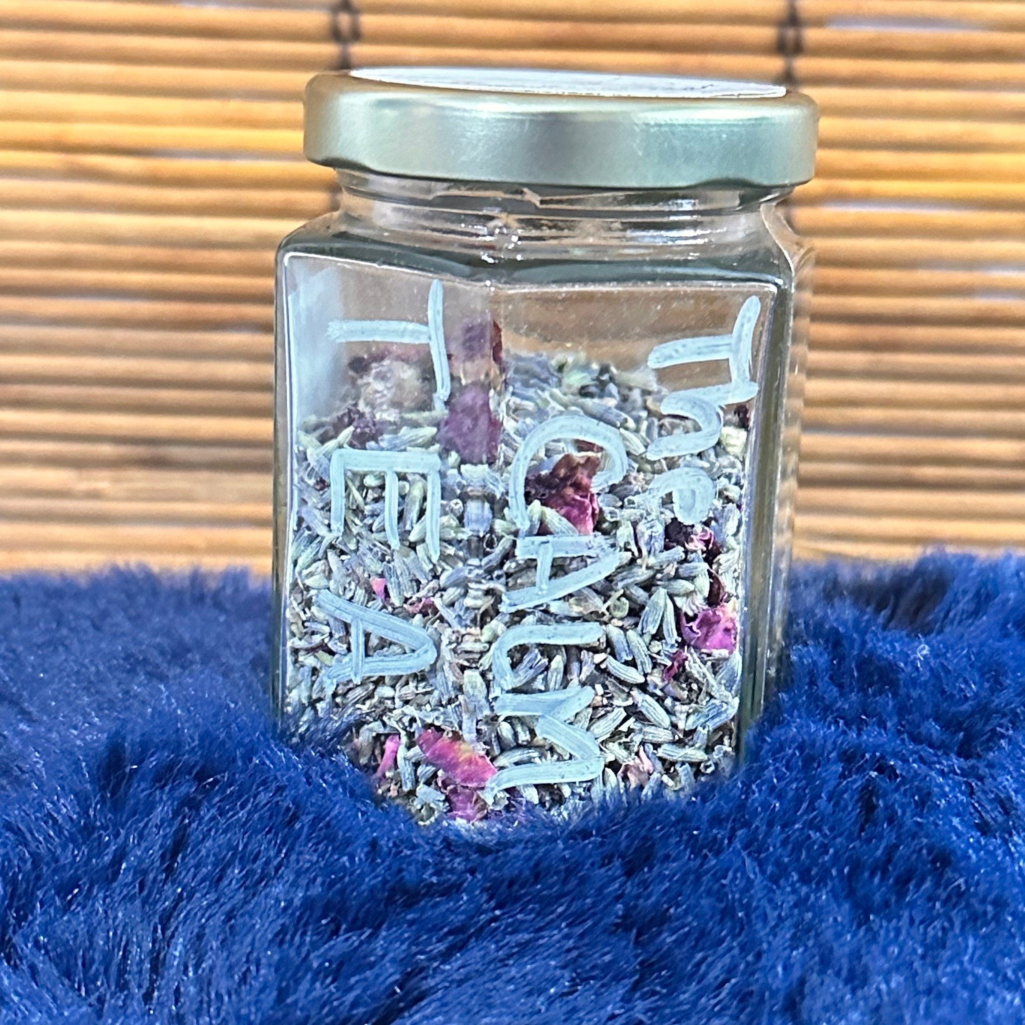 Jar of lavender and rose petals, clear glass container with light blue text, on blue fuzzy fabric