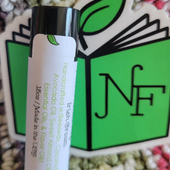 Lip balm tube with black cap and white label, green leaf logo, and text on a green background