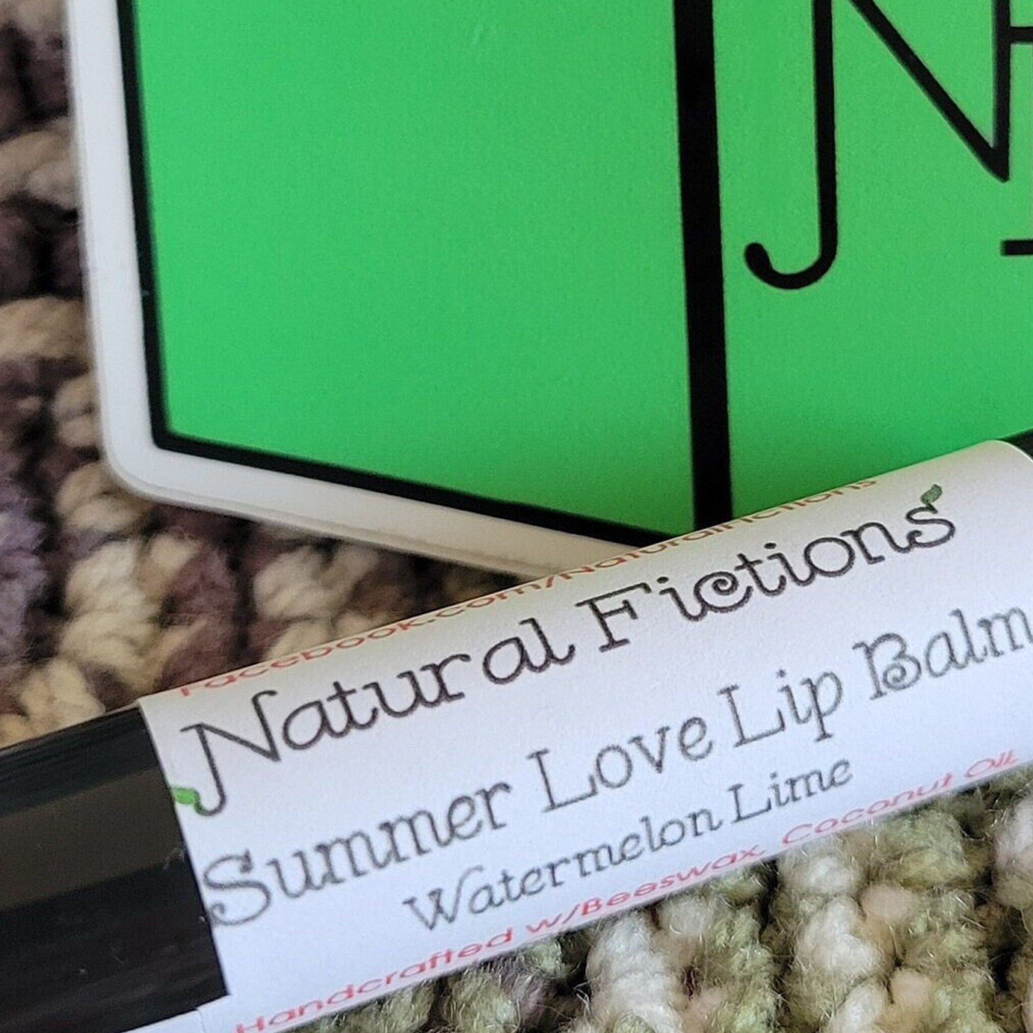 Lip balm tube with white label, black text, and green background, Natural Fictions brand