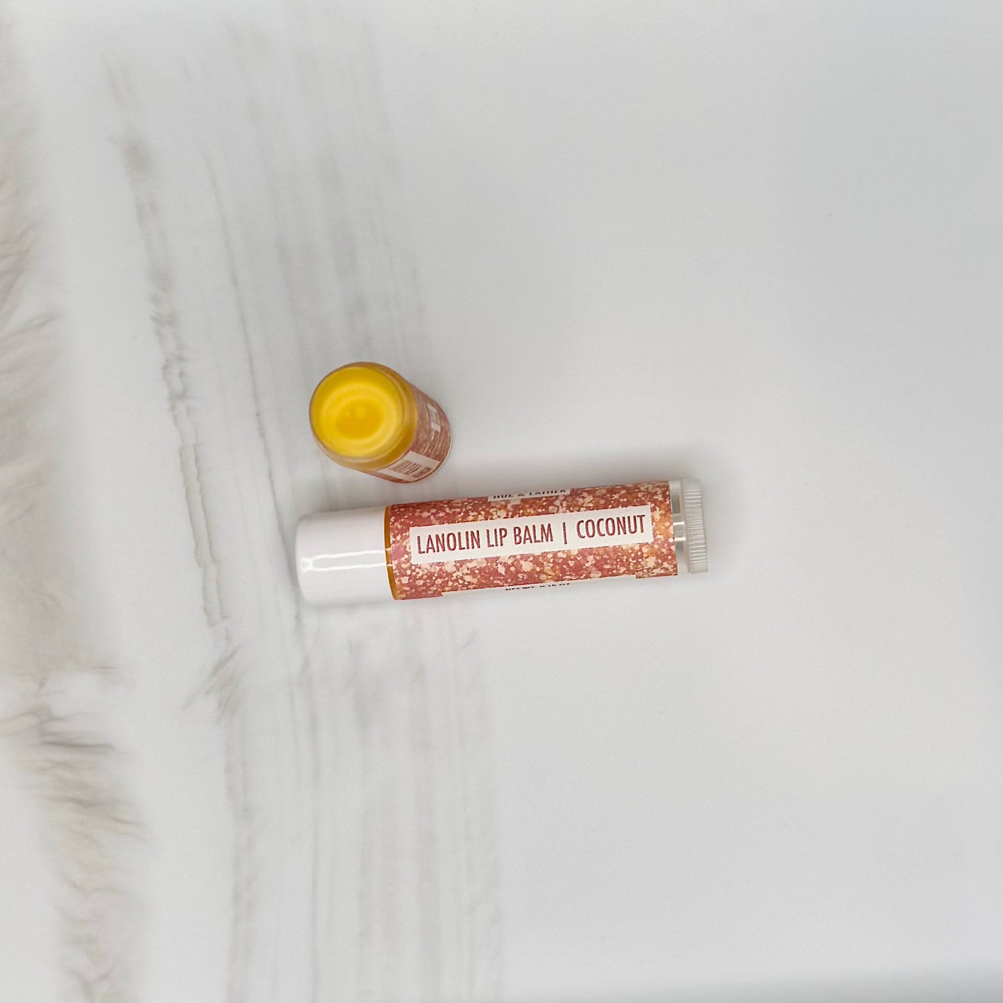 Lip balm tubes and container with white and glittery brown labels, yellow balm visible