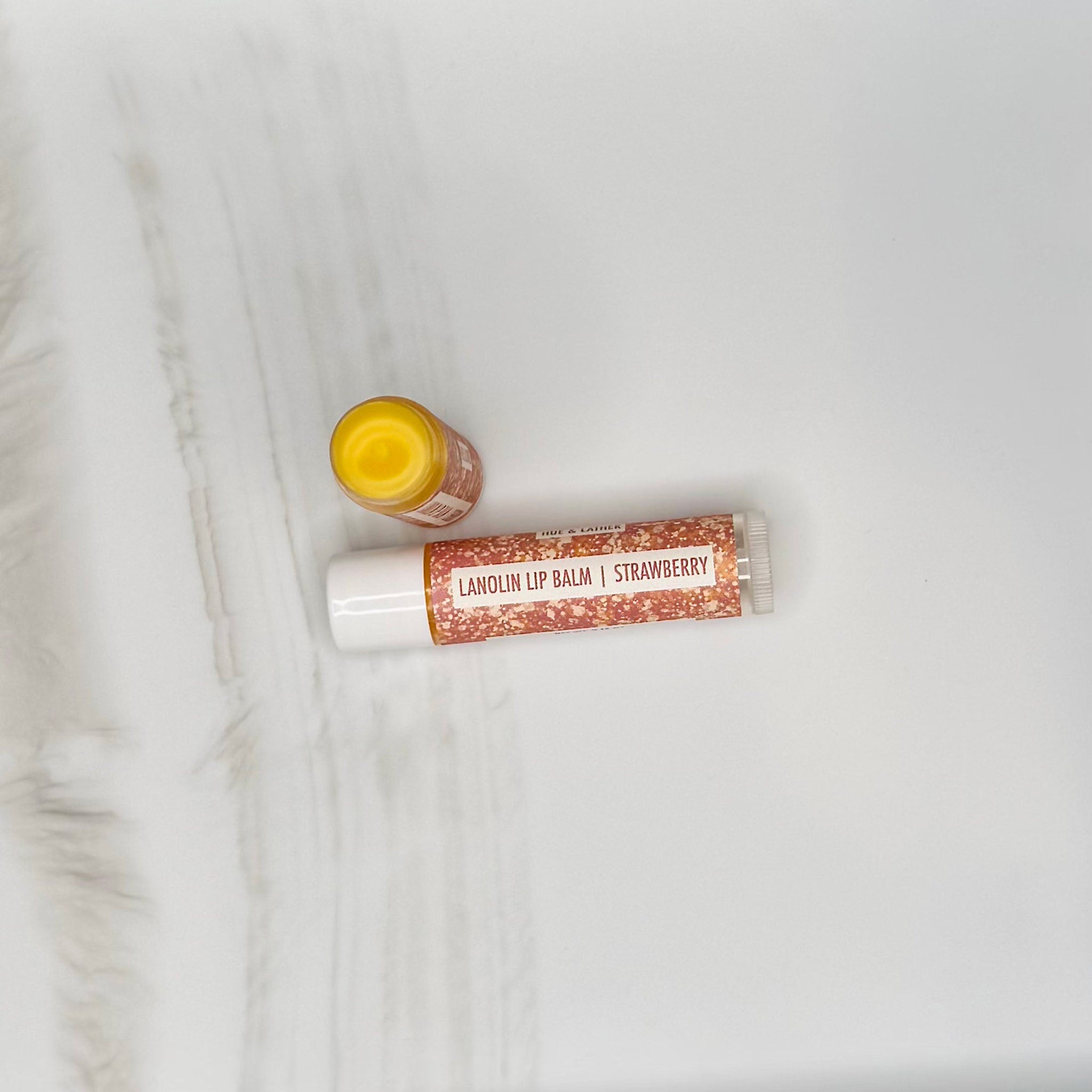 Lanolin lip balm with white tube, orange glitter pattern, and yellow balm inside