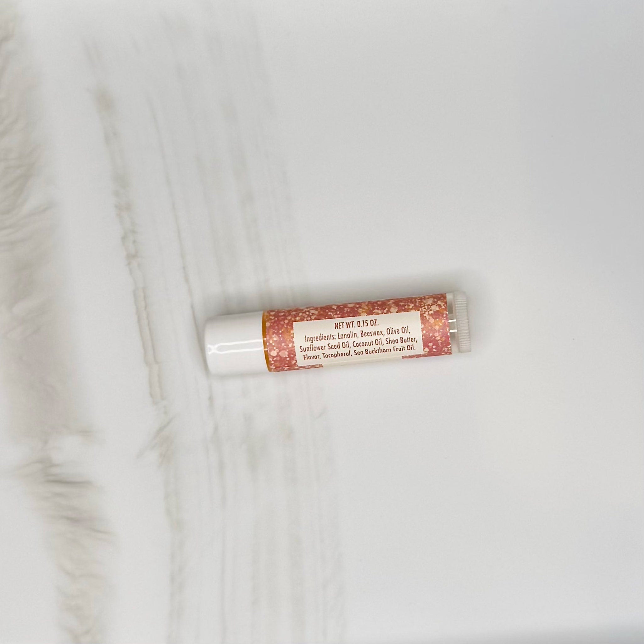 Lip balm tube with white and speckled pink pattern, Hue & Lather branding visible on the label
