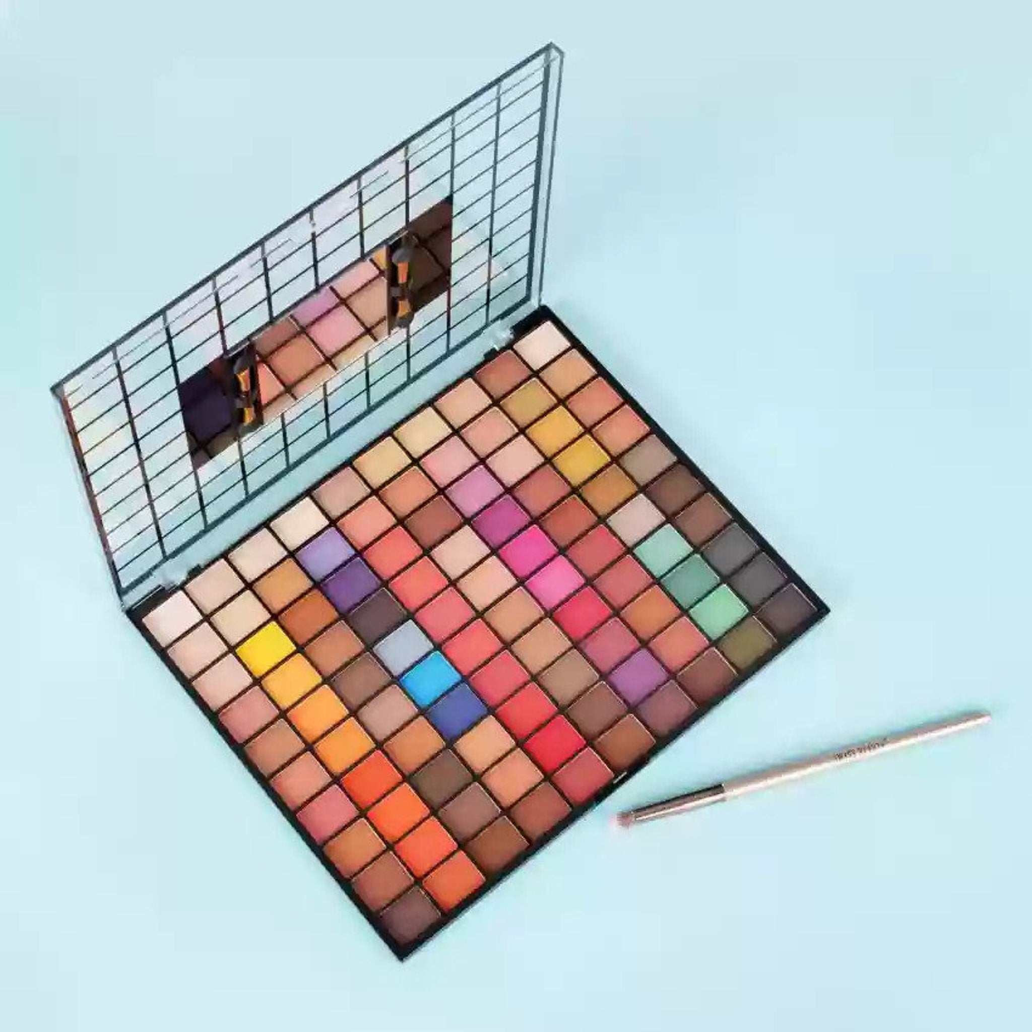Eyeshadow palette with multiple colorful squares, black frame, and a brush on a blue surface