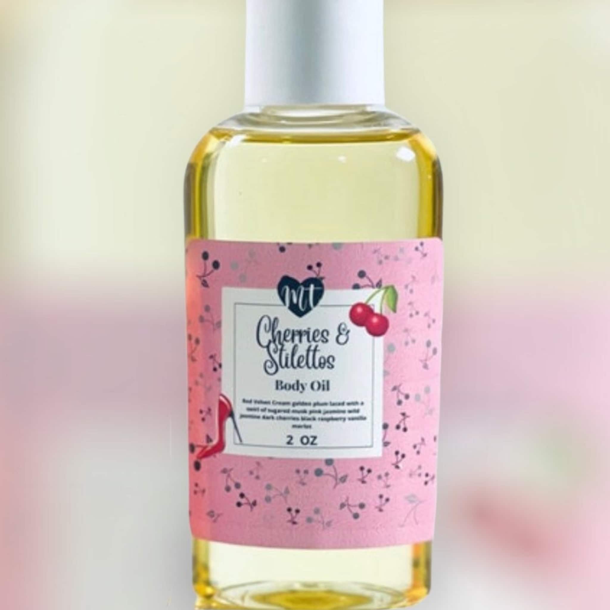 Body oil bottle with yellow liquid, white cap, and pink label with Cherries & Stilettos text