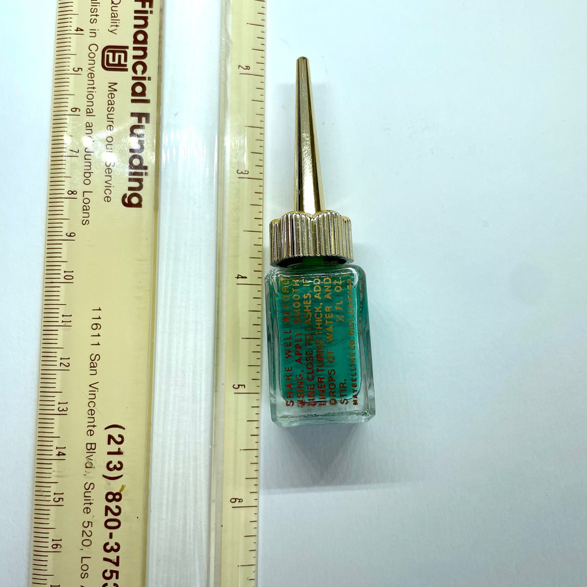 Side view of vintage green eyeliner in glass bottle with golden spire lid, showcasing tapered shape and label details
