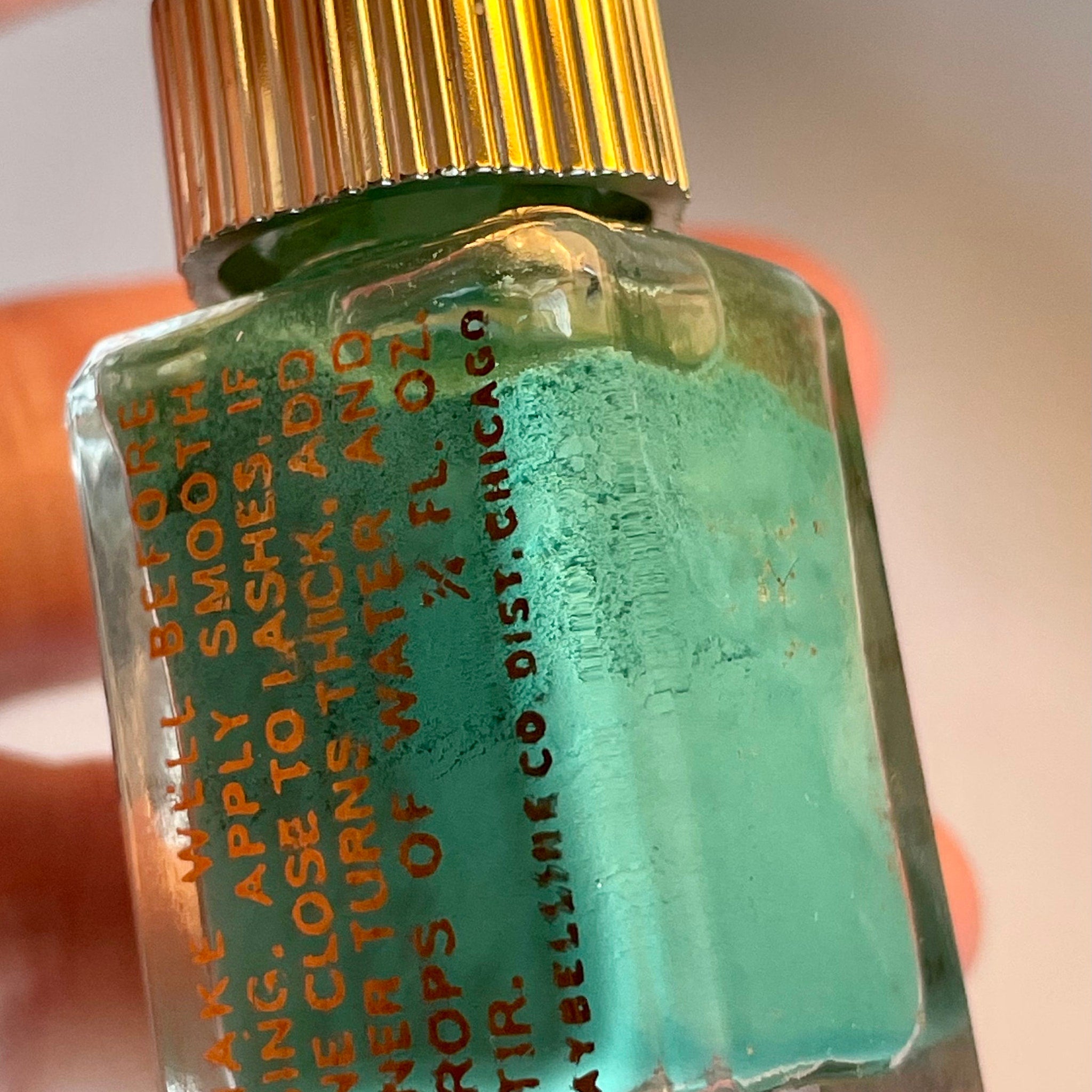 Side view of vintage Maybelline green fluid eyeliner in glass bottle with golden spire lid, showcasing tapered shape